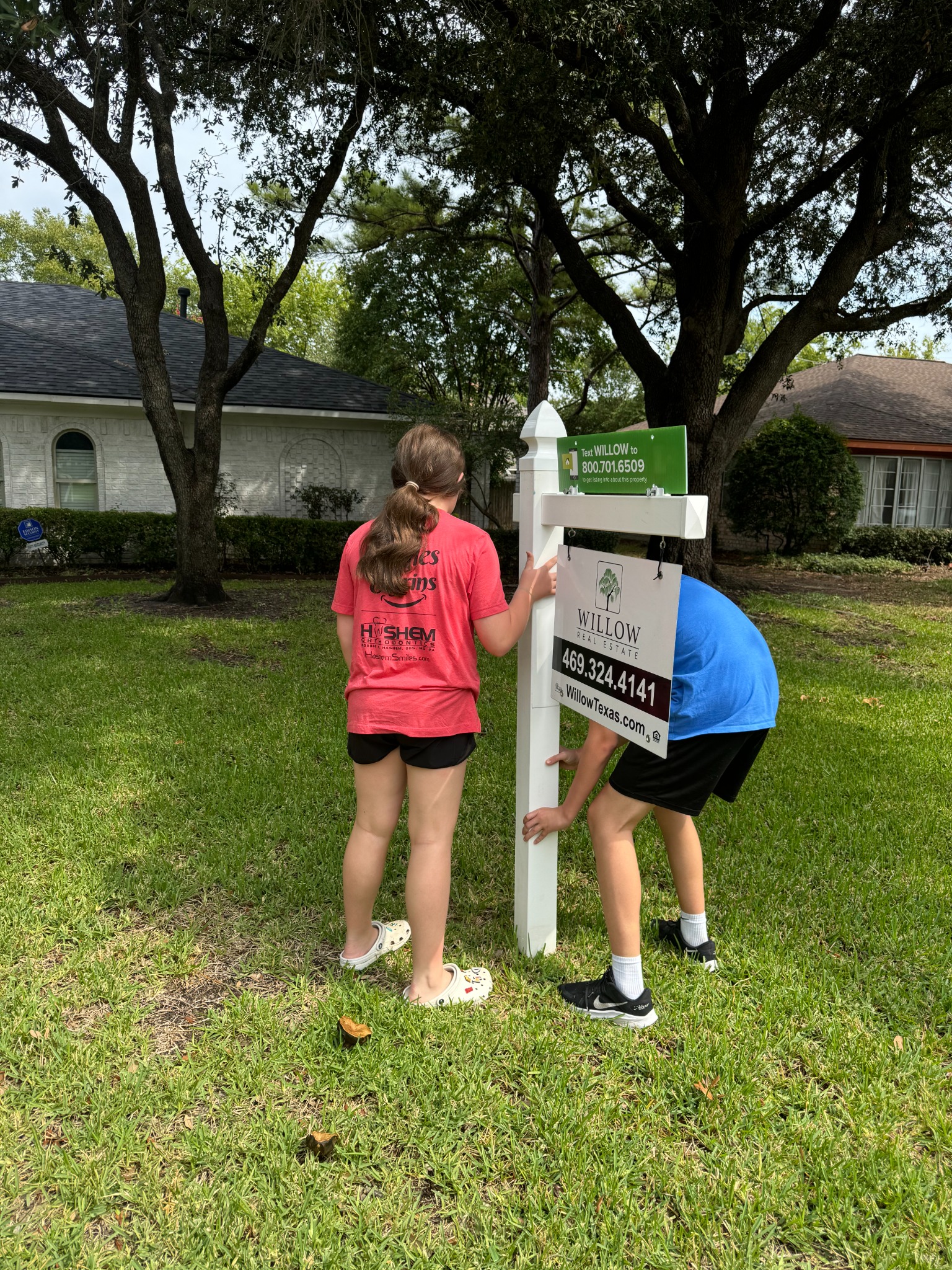 Two people setting a Willow Real Estate sign outside a Texas home